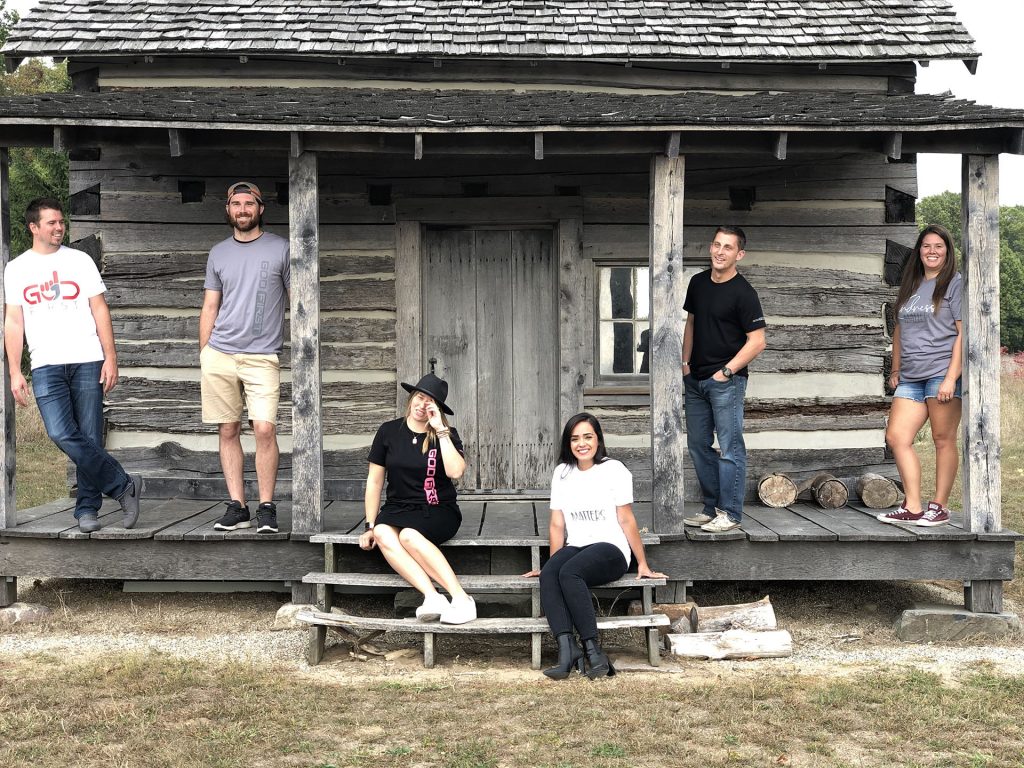 six people standing on a porch of a small old house.